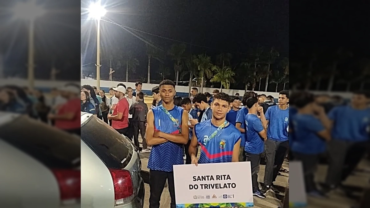 Dois jovens atletas de vôlei de areia com uniformes azuis, segurando uma placa com o nome Santa Rita do Trivelato, ao lado de outras pessoas em um evento esportivo. Crédito: Instagram Santa Rita Do Trivelato.
