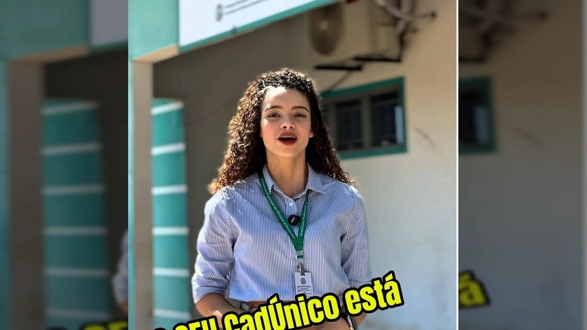 Mulher sorrindo em frente ao CRAS Nenice Pereira Leite, com crachá da Prefeitura de Mirassol d'Oeste - MT, explicando sobre o Cadastro Único