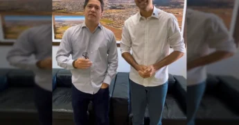 Dois homens, representando a Prefeitura de Campo Verde e o Cartório Eleitoral, em frente a um quadro com vista aérea da cidade, firmando acordo para cadastramento biométrico / Instagram @prefcampoverde