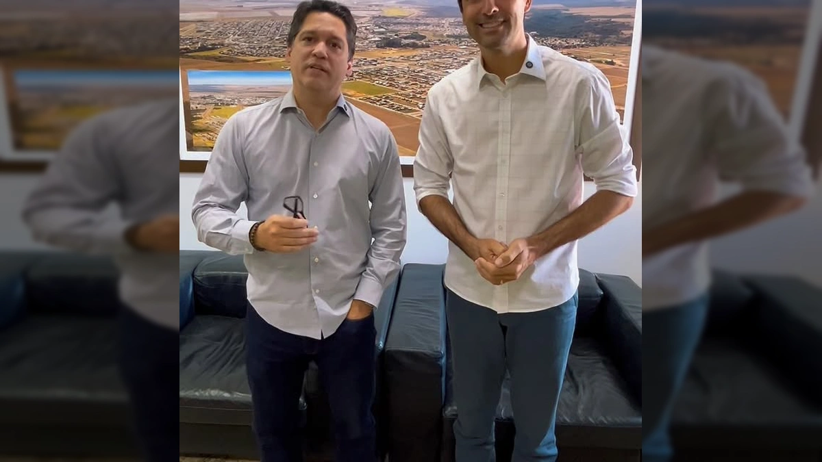 Dois homens, representando a Prefeitura de Campo Verde e o Cartório Eleitoral, em frente a um quadro com vista aérea da cidade, firmando acordo para cadastramento biométrico / Instagram @prefcampoverde