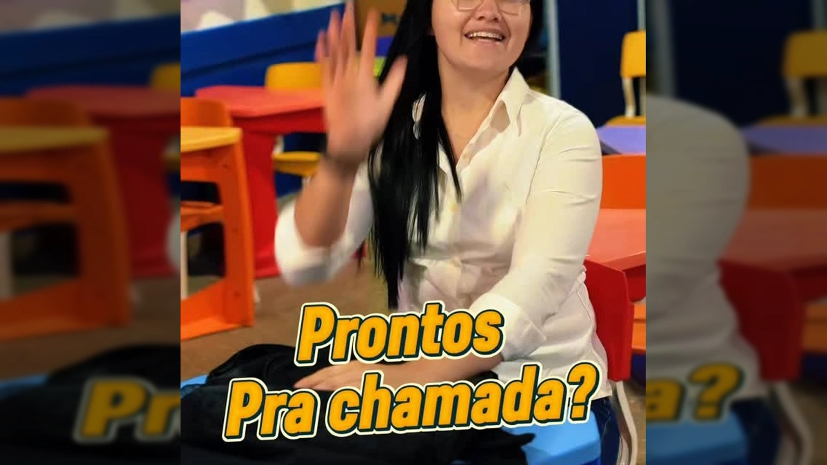 Professora com óculos e cabelo escuro sorrindo, com um quadro de boas-vindas de volta às aulas ao fundo, na Prefeitura Municipal de Guarantã do Norte / Instagram.