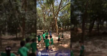 Crianças em uniformes verdes plantando mudas no Viveiro Municipal de Matupá, com adultos da SEMMA orientando. Crédito: Prefeitura Municipal de Matupá / Instagram.