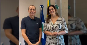 Duas pessoas, um homem e uma mulher, em um ambiente de escritório com bandeiras ao fundo, falando sobre o encontro de saúde em Lucas do Rio Verde. Crédito: Secretaria de Saúde de Lucas do Rio Verde/MT