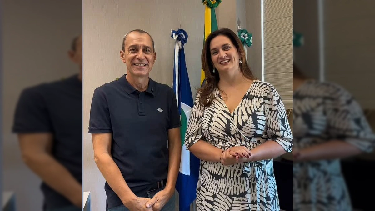 Duas pessoas, um homem e uma mulher, em um ambiente de escritório com bandeiras ao fundo, falando sobre o encontro de saúde em Lucas do Rio Verde. Crédito: Secretaria de Saúde de Lucas do Rio Verde/MT