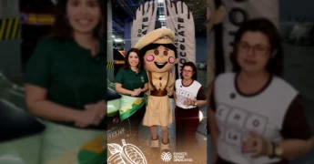 Mulher sorrindo em evento de chocolate com mascote da Famato. Crédito: Senar-MT / Instagram