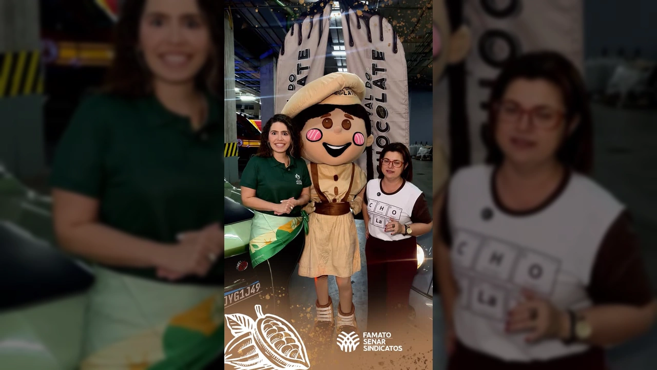 Mulher sorrindo em evento de chocolate com mascote da Famato. Crédito: Senar-MT / Instagram