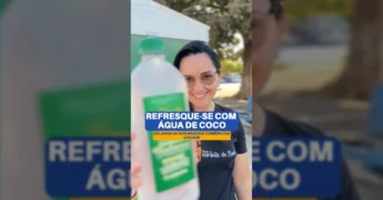 Foto de uma mulher bebendo água de coco, com o banner da 'Água do Baiano' ao fundo, promovendo produto local em Guarantã do Norte. Créditos: Prefeitura Municipal.