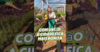 Uma mulher sorridente em pé em um viveiro, cercada por plantas jovens, enquanto outras pessoas trabalham ao fundo, com texto 'OI PESSOAL' e 'ASSISTÊNCIA SOCIAL'. Crédito: Prefeitura de Nova Bandeirantes / Instagram.