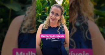 Mulher com cabelo loiro encaracolado e óculos, vestindo um vestido azul-marinho, sorrindo e gesticulando em frente a uma folhagem verde. Créditos: Instagram / sebraematogrosso