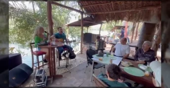 Banda tocando música raiz ao vivo em um rancho às margens do Rio Manso, com pessoas desfrutando de churrasco de Angus. Créditos: Instagram @ranchodomano.