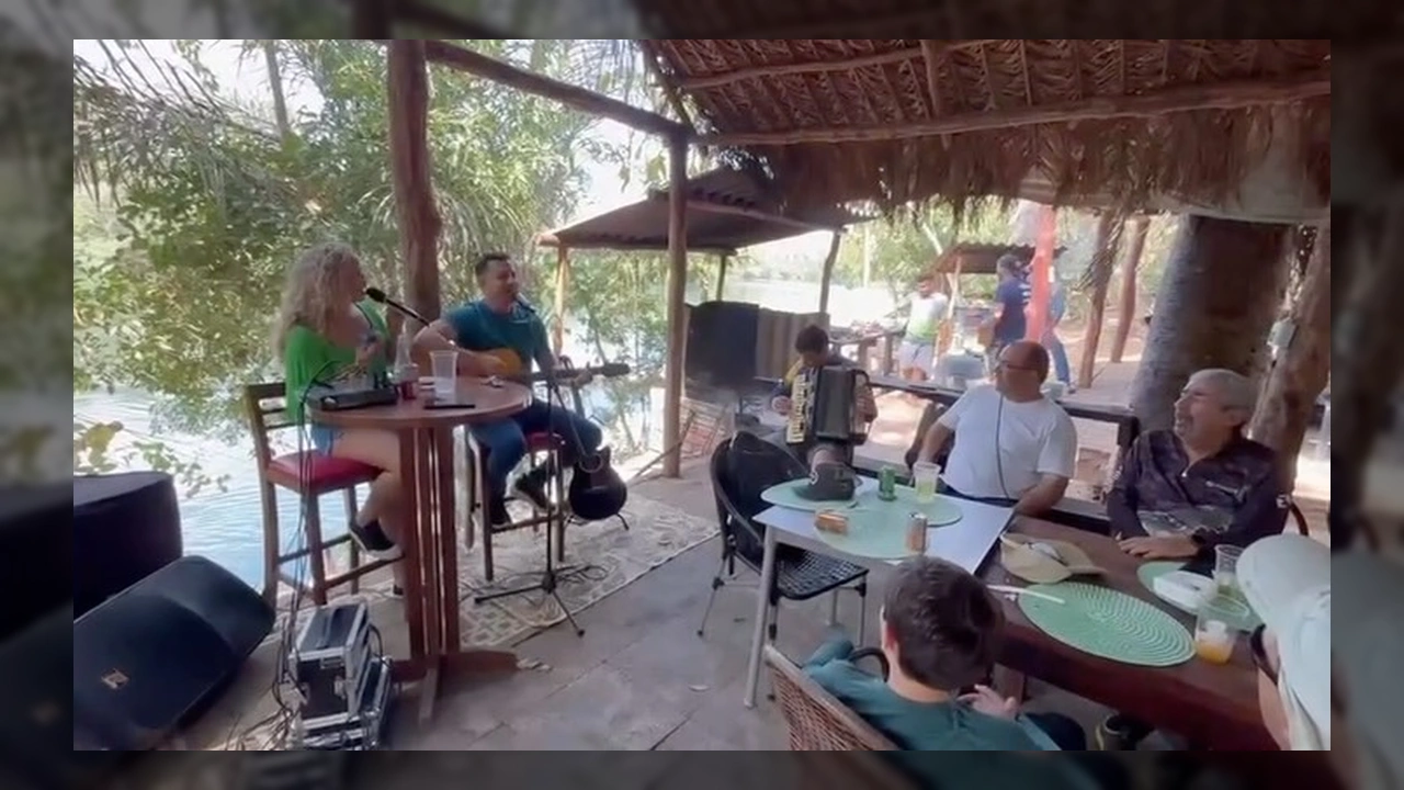 Banda tocando música raiz ao vivo em um rancho às margens do Rio Manso, com pessoas desfrutando de churrasco de Angus. Créditos: Instagram @ranchodomano.