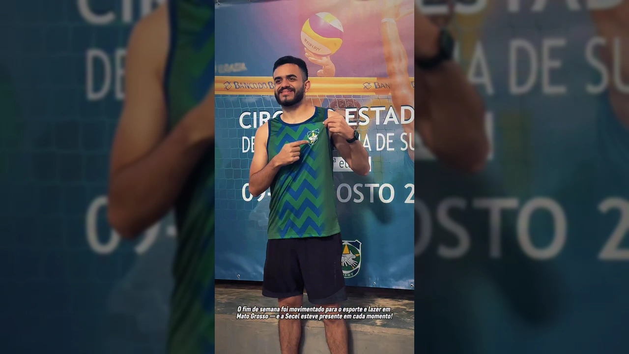 Homem sorrindo e apontando para a camisa com o logo da Federação Mato-grossense de Desportos de Surdos, em evento de vôlei de praia para surdos, com créditos para SecelMT no Instagram