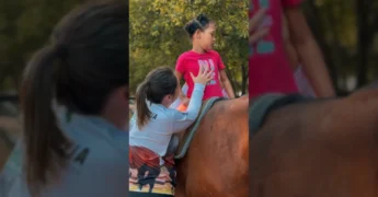 Criança Ayla em cima de um cavalo durante sessão de equoterapia com apoio de dois terapeutas do Sindicato Rural de Pedra Preta
