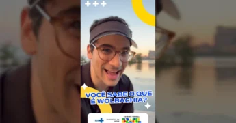 Homem com óculos e visor, gesticulando com o dedo indicador para um mosquito Aedes aegypti com uma seringa verde inserida. O fundo é um pôr do sol sobre a água. Créditos: Ministério da Saúde / Instagram