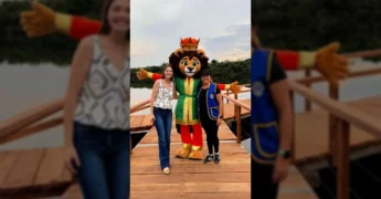 Duas mulheres e o mascote Leão Alegrito em um deck de madeira em Sapezal, promovendo o Festival de Pesca. Créditos: lionssapezal / Instagram