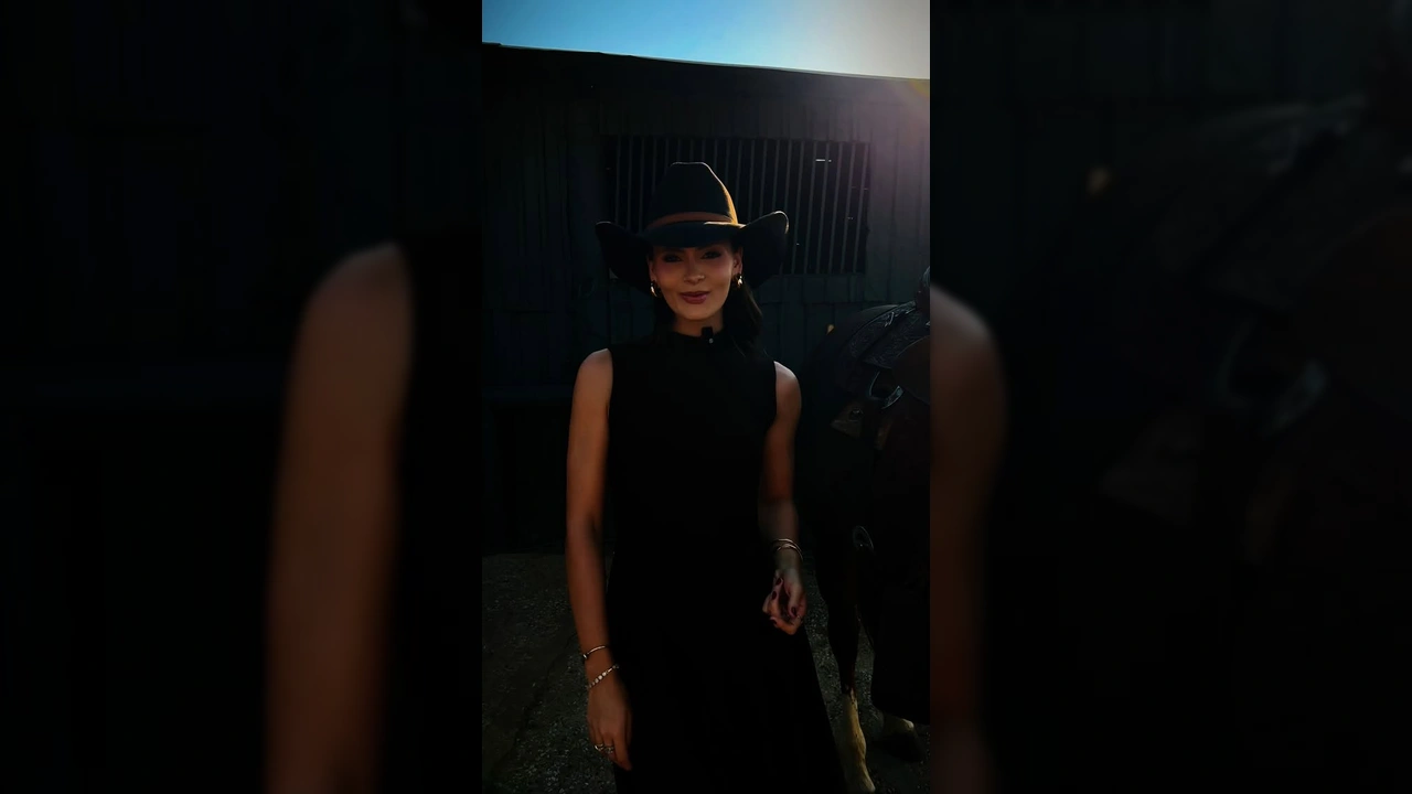 Mulher vestida de cowgirl com chapéu preto, vestido marrom, falando sobre a Expo Diamantino 2025. Créditos: expodiamantino / Instagram