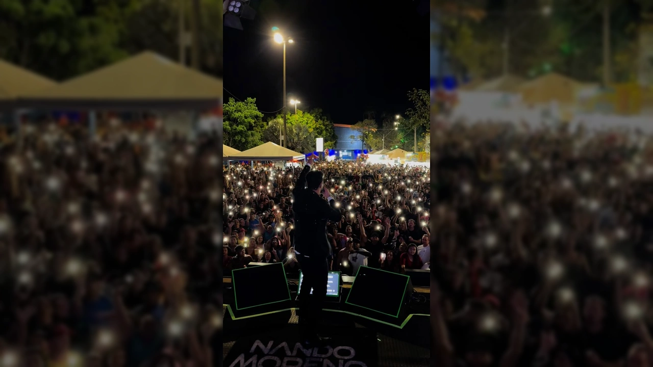 Nando Moreno se apresentando em palco para uma multidão com luzes de celulares acesas, no Porto do Baé, Barra do Garças. Créditos: Prefeitura de Barra do Garças / Instagram.